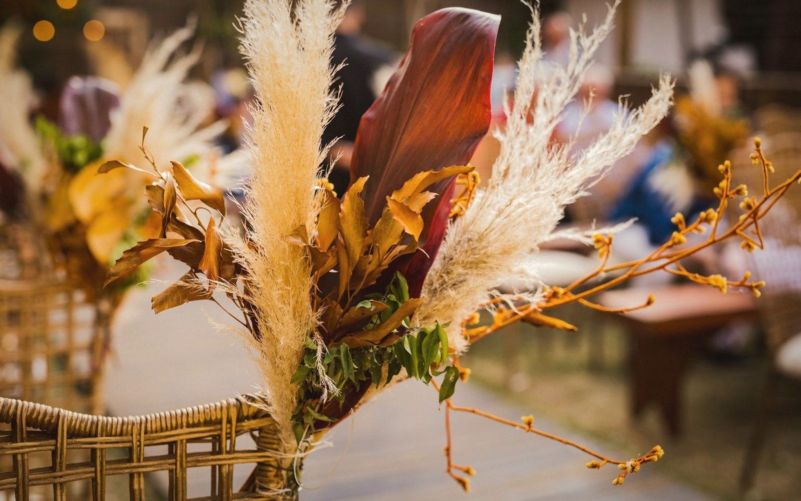 Pampas grass and dried leaves tied to a wicker chair back at an outdoor event