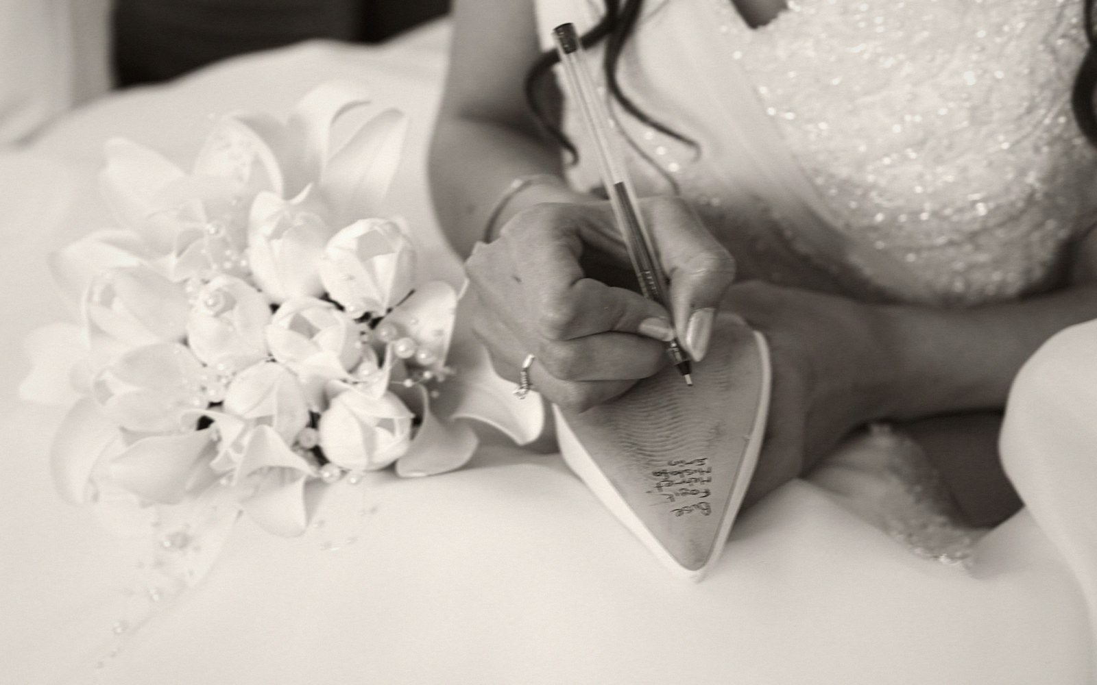 A bride writes a note on the sole of her shoe beside her bouquet