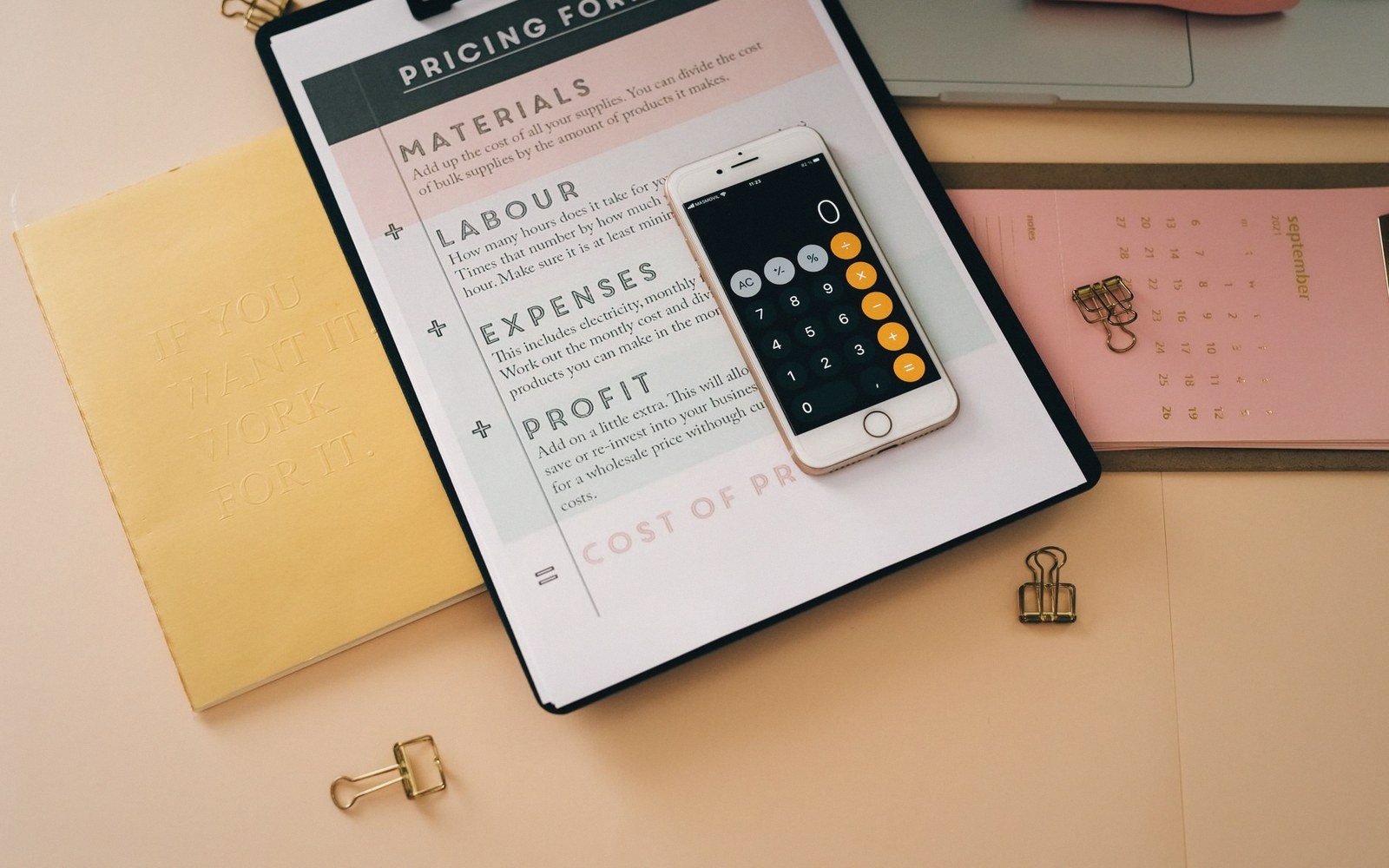Smartphone calculator app resting on a pricing formula worksheet with notebooks and clips