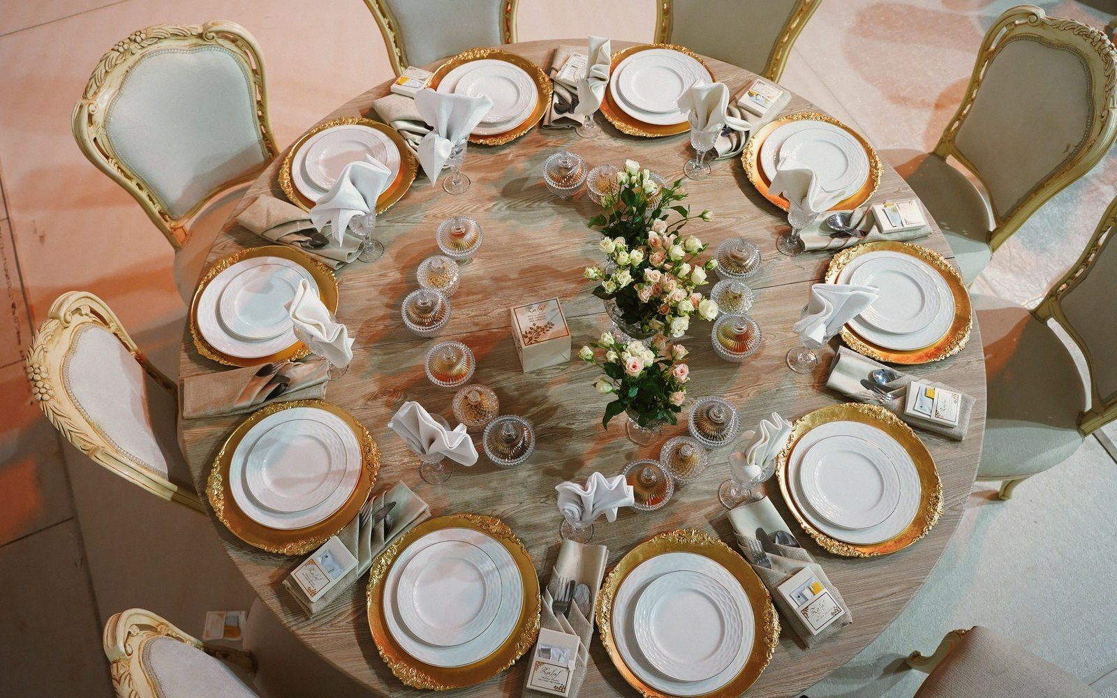 Overhead view of a round table set with gold-rimmed plates, folded napkins and a floral centerpiece
